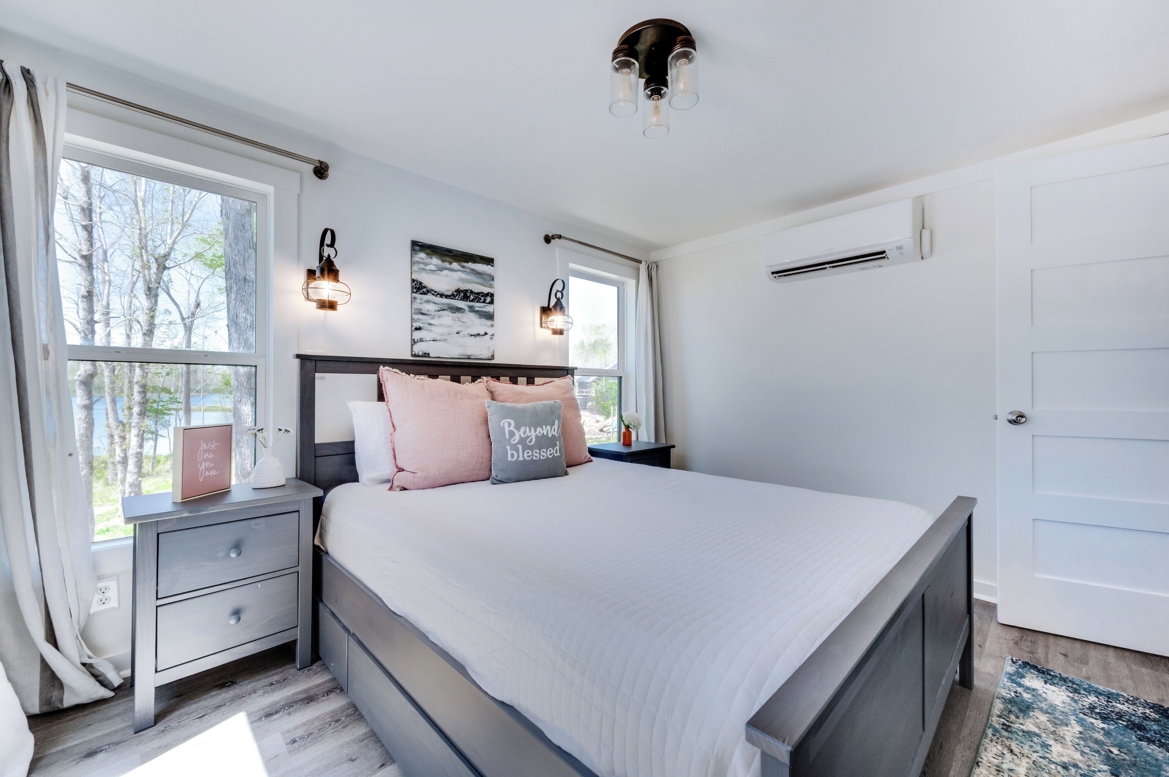 A bedroom with a bed, bedside tables, a nightstand, a wall-mounted lamp, and a window with curtains.