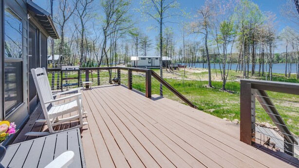 Terraza de madera con mobiliario exterior, con vistas a un lago rodeado de árboles.