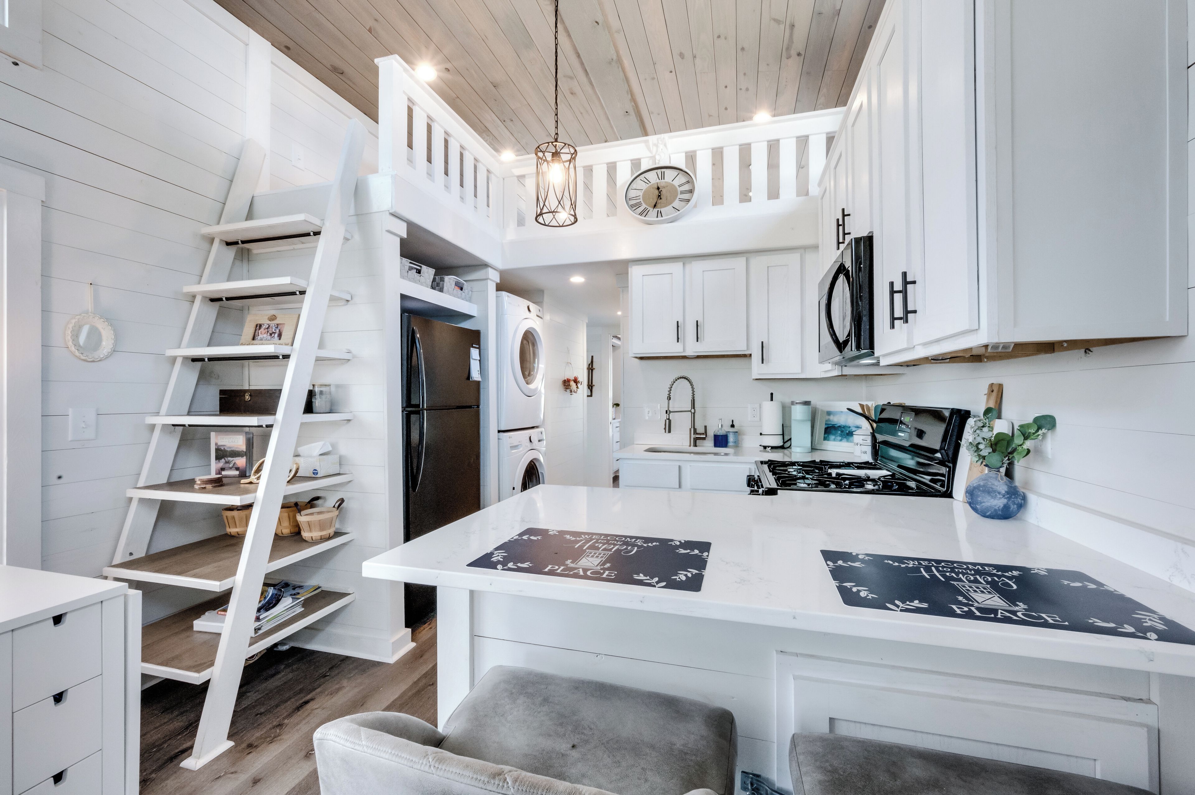 A modern kitchen with white cabinetry, a built-in washer and dryer, a gas stove, and a wooden ceiling.
