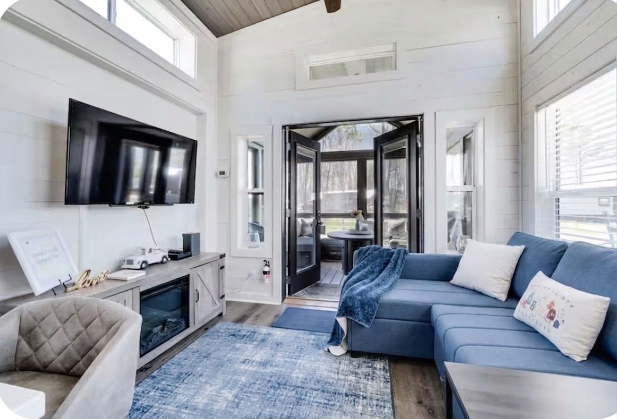 A modern living room with a flat-screen TV, a blue sofa, a cushioned armchair, and a coffee table.
