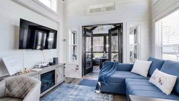 A modern living room with a flat-screen TV, a blue sofa, a cushioned armchair, and a coffee table.