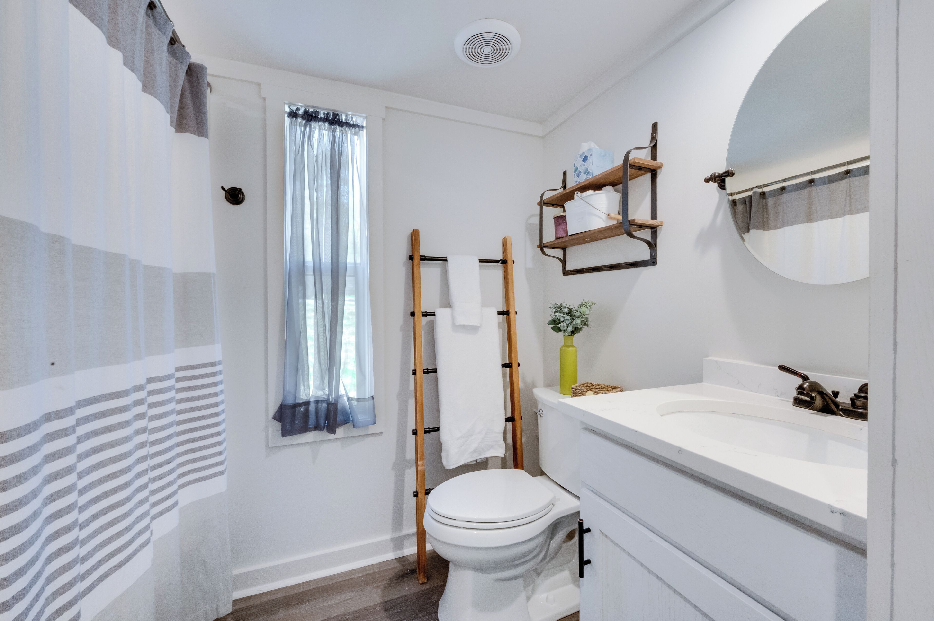 Un bagno con il water, un lavandino, uno specchio, una finestra con tende leggere e un porta asciugamani.