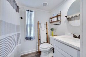 Un bagno con il water, un lavandino, uno specchio, una finestra con tende leggere e un porta asciugamani.