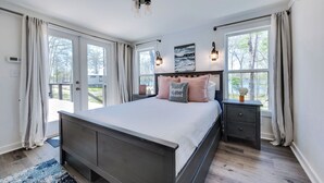 Un dormitorio con una cama grande, una mesita de noche, una lámpara de pared y un ventanal con cortinas.