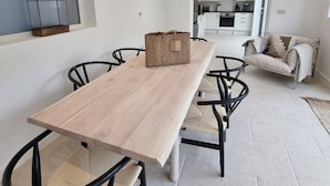 Uma zona de refeições moderna com uma mesa de madeira e cadeiras pretas, um cesto sobre a mesa, e vista para uma cozinha e zona de estar.