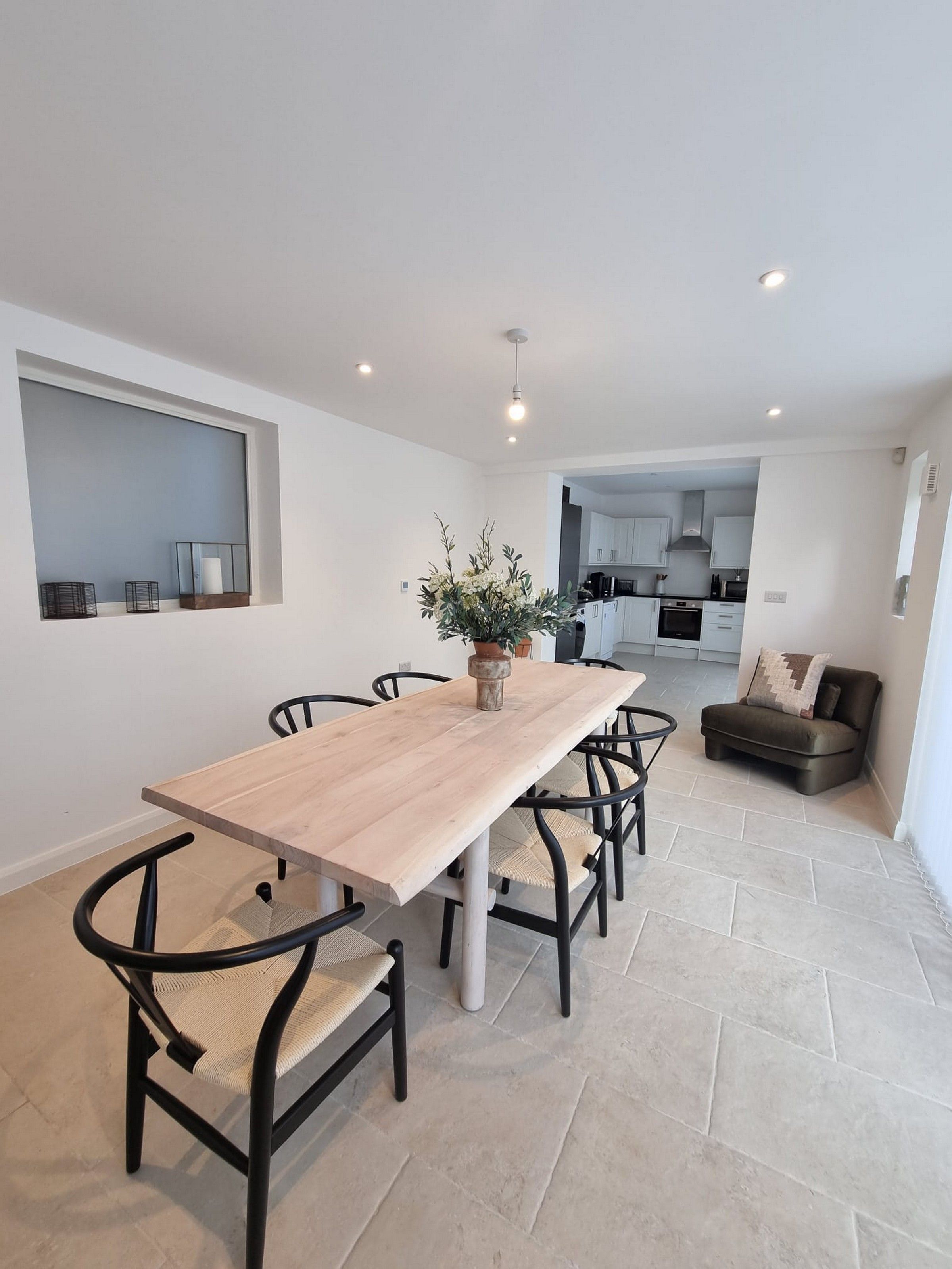 A modern dining area with a wooden table and black chairs, a potted plant, and a view into the kitchen.