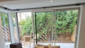 Uma sala de estar moderna com um sofá bege, um tapete estampado e vista para um jardim através de grandes portas de vidro deslizantes.