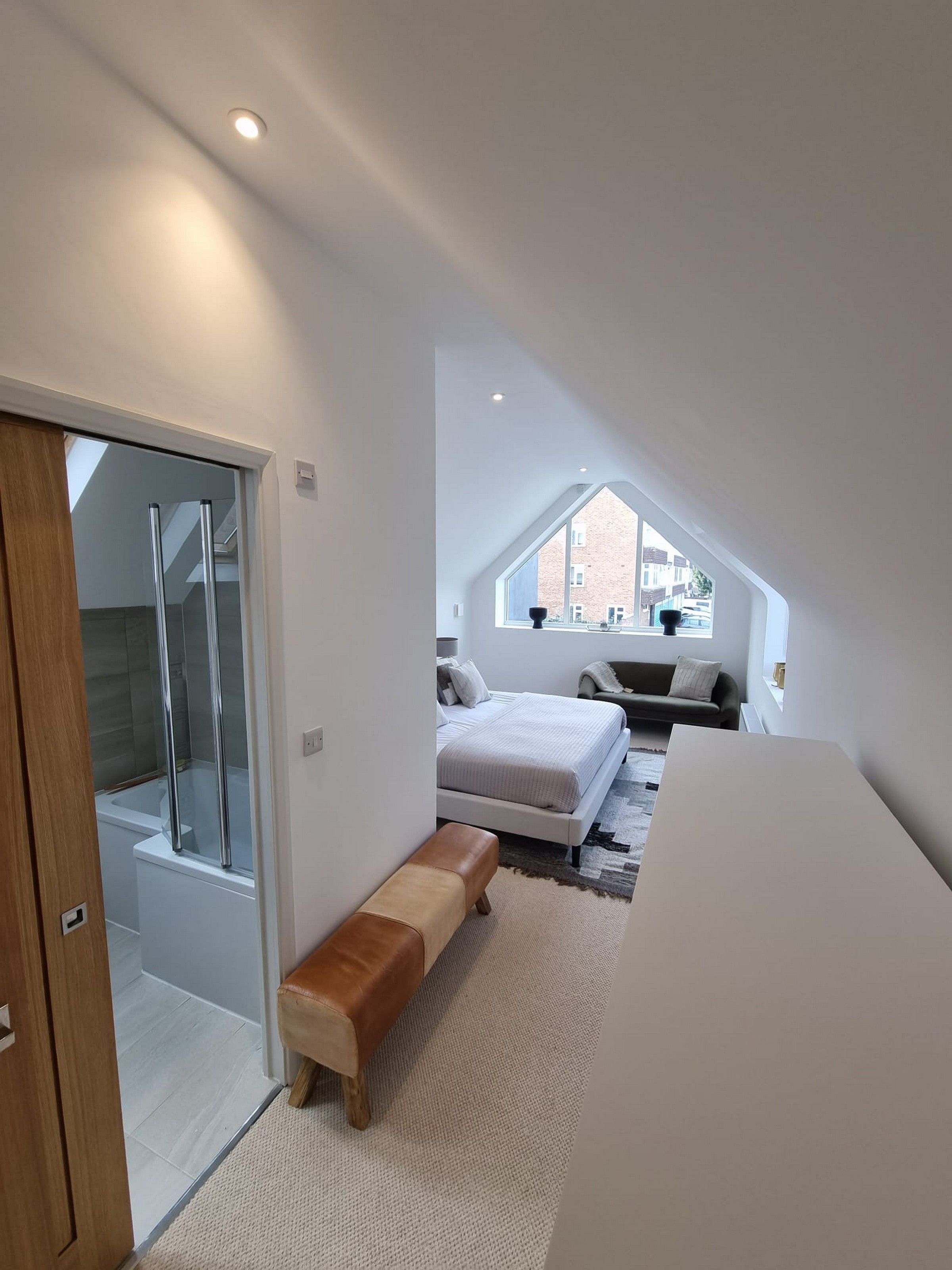 A modern bedroom with a skylight, a bed, a bench, and a shower area.
