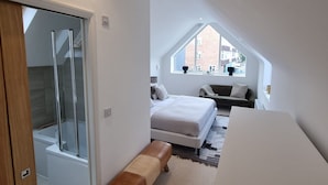 Quarto moderno com claraboia, uma cama, um banco e área de chuveiro.