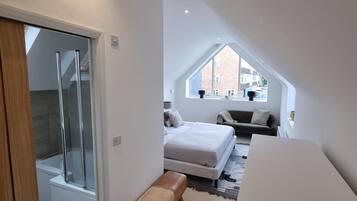 A modern bedroom with a skylight, a bed, a bench, and a shower area.