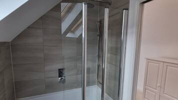A modern bathroom with a glass-enclosed shower, a bathtub, and a skylight above.