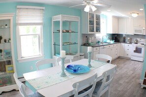 A kitchen with white cabinets, a dining table with chairs, and a ceiling fan. - Bonnet Shores Getaway, 3BR, 10 min Walk to Private Beach (Narragansett)