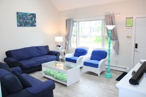 A living room with a blue sofa, two armchairs, a coffee table, and a floor lamp. - Bonnet Shores Getaway, 3BR, 10 min Walk to Private Beach (Narragansett)