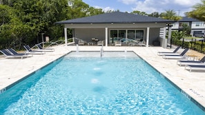 A rectangular swimming pool with clear blue water, surrounded by lounge chairs and a covered seating area with a roof.