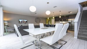Una cocina moderna con comedor, que incluye una mesa blanca grande, sillas blancas y un refrigerador de acero inoxidable.