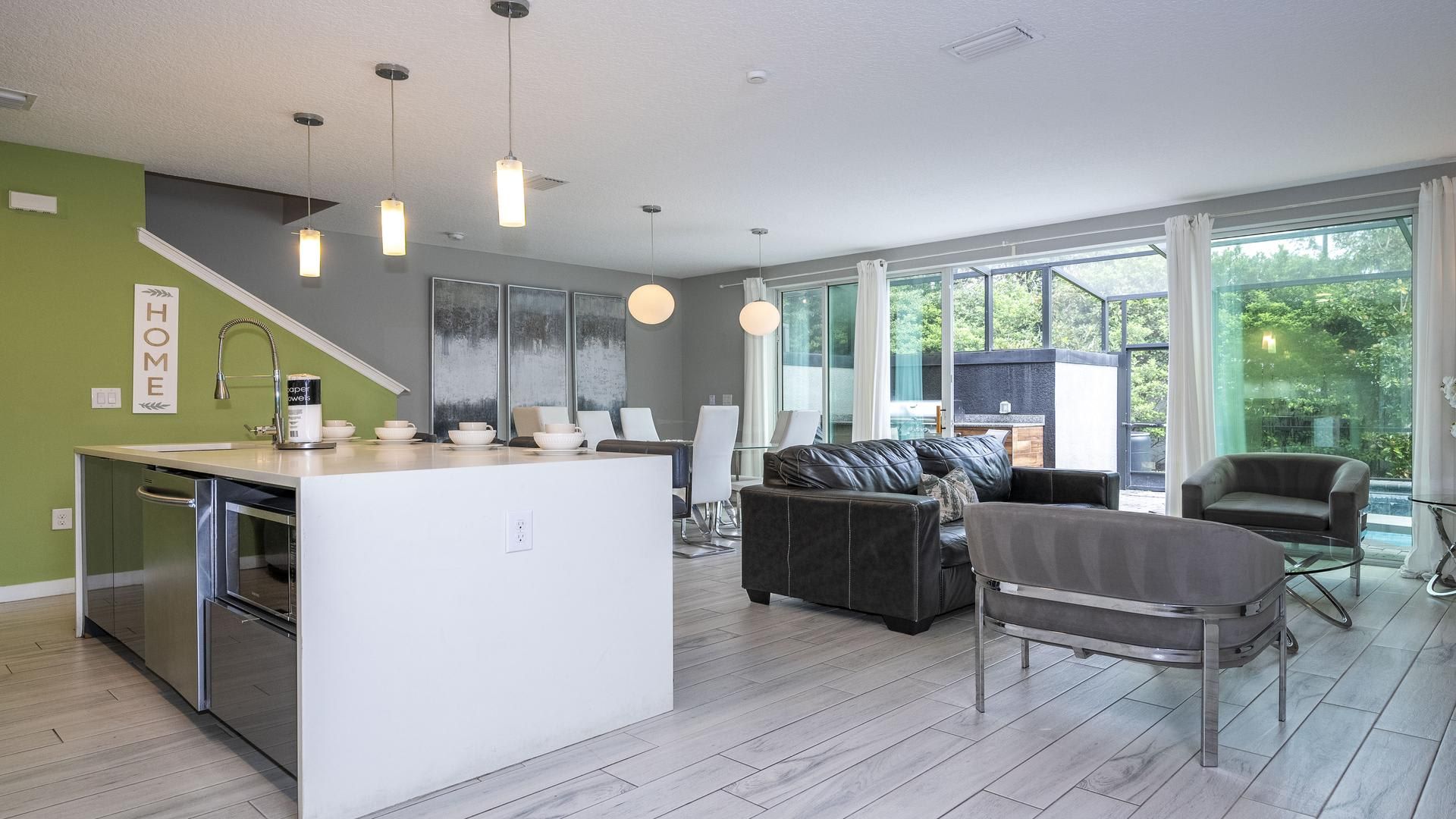 Een moderne keuken met een centraal eiland, een eethoek met stoelen, een bank en een groot raam met gordijnen.
