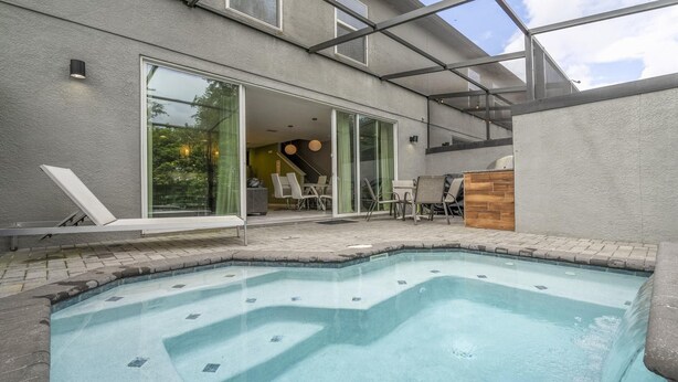 A modern outdoor swimming pool area with a glass-enclosed patio, lounge chairs, and a wooden deck.
