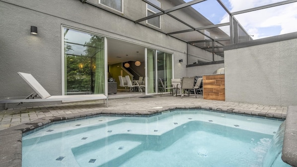 A modern outdoor swimming pool area with a glass-enclosed patio, lounge chairs, and a wooden deck.