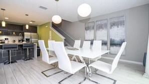 A modern kitchen with stainless steel appliances, a dining area with white chairs and a glass table, and a staircase leading to a loft.
