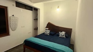 Quarto com cama, ventoinha no teto, luminária na parede e porta.