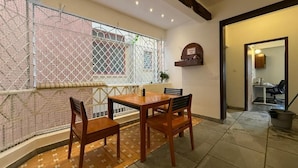 Uma área de refeições com mesa e cadeiras, uma janela com grade de metal e uma pequena estante com um letreiro.