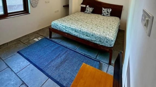 Quarto com cama, ventoinha no teto, mesa de cabeceira e janela.