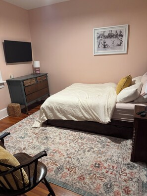 Una camera da letto con un letto, una cassettiera, una sedia, un tappeto, una televisione e un quadro appeso al muro.