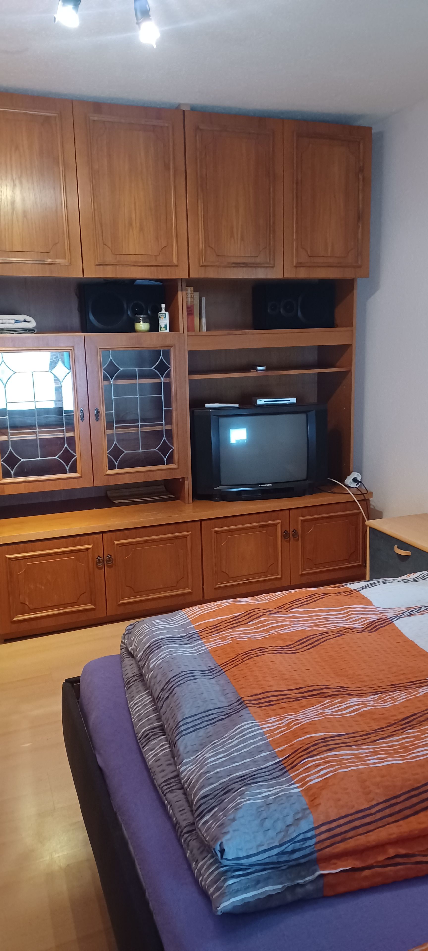 A bedroom with a bed, wooden cabinets, a television, and a window with decorative glass.