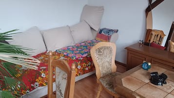A room with a bed, a chair, a small table, a mirror, and a potted plant.