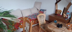 A room with a bed, a chair, a small table, a mirror, and a potted plant.