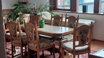 A dining area with a wooden table and chairs, a patterned rug, and potted plants.