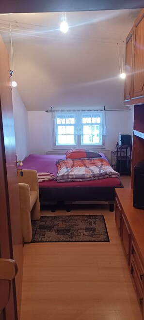 A bedroom with a bed, a chair, a desk, and a window.