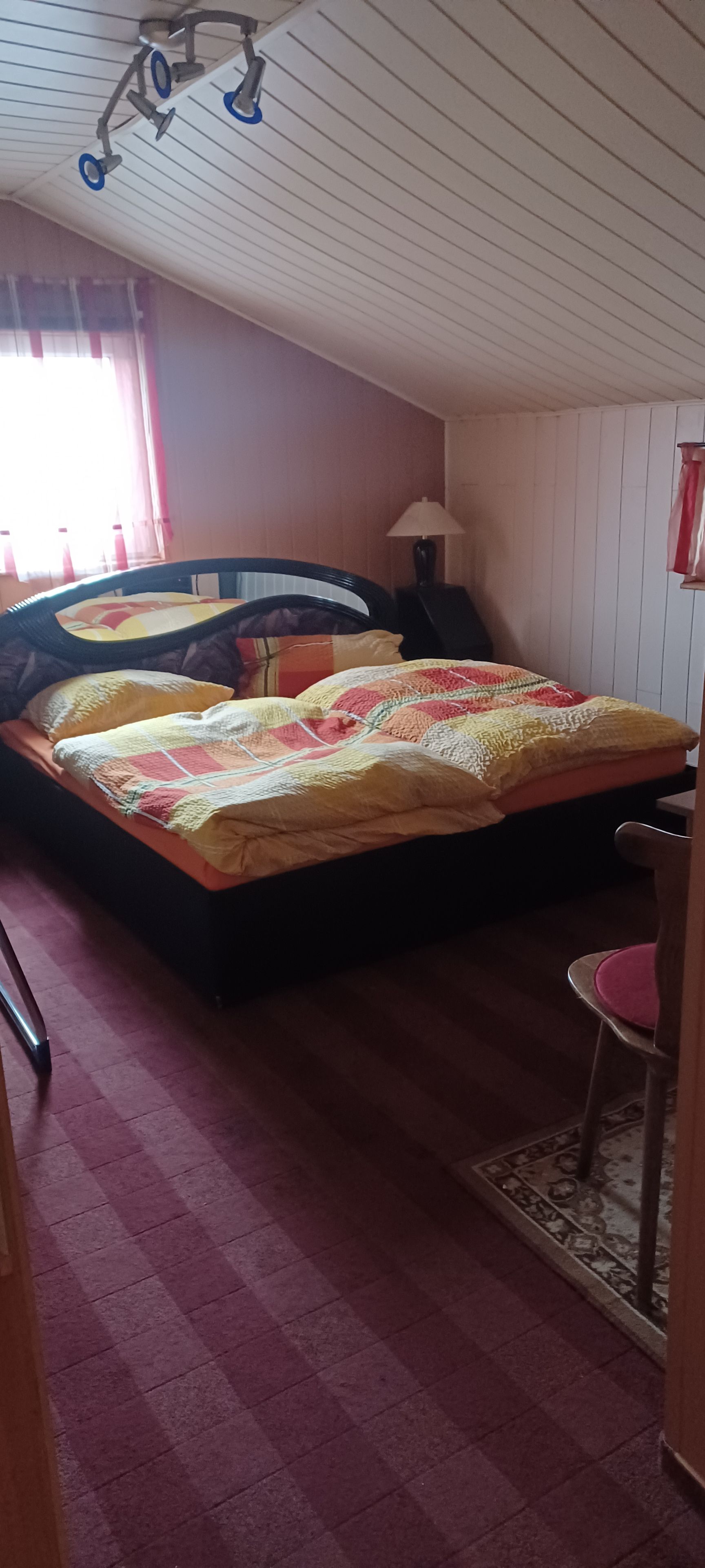 A bedroom with a bed, a chair, a lamp, and a window with curtains.