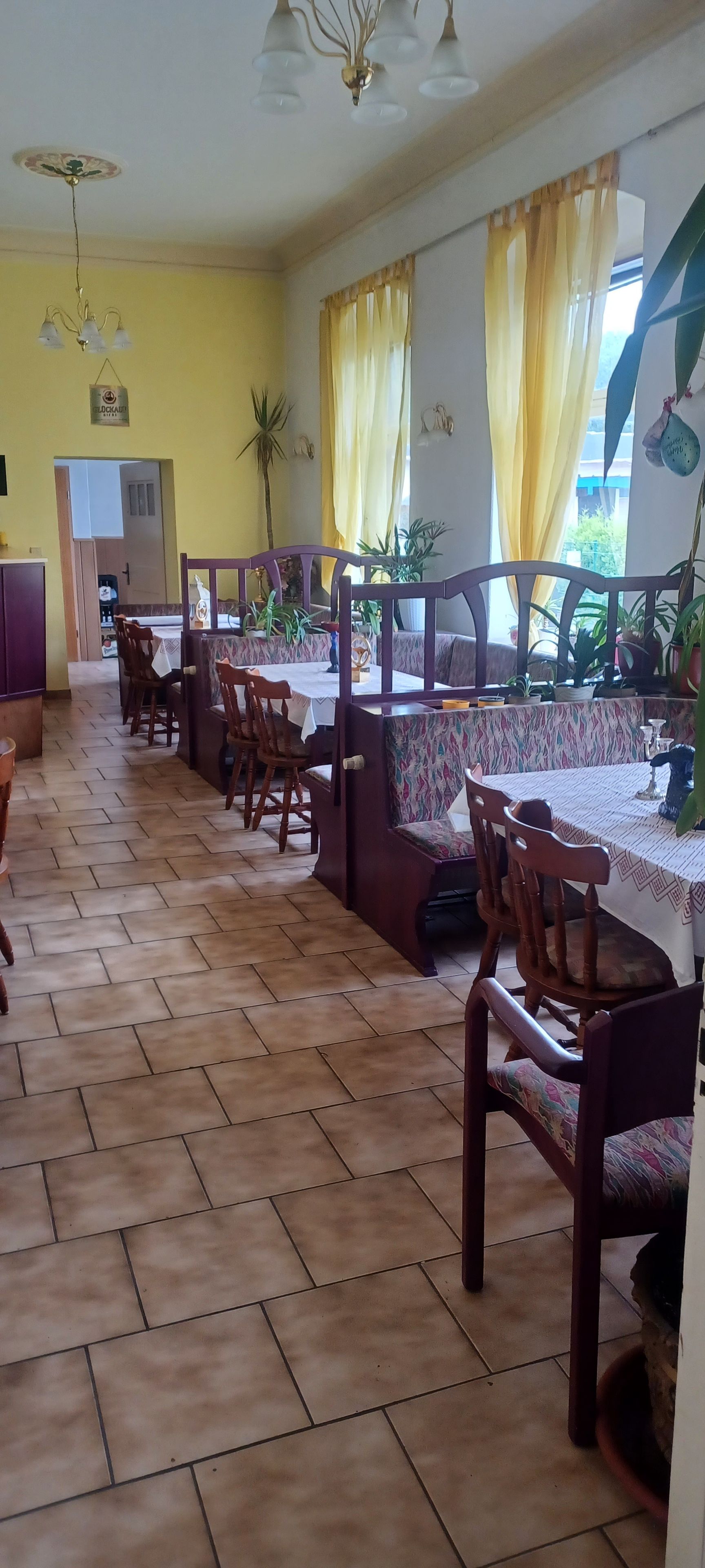 A dining area with wooden chairs and tables, yellow curtains, and potted plants.