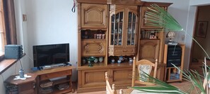 Un mueble de madera con puertas de cristal, un televisor sobre un soporte de madera y una planta al frente.