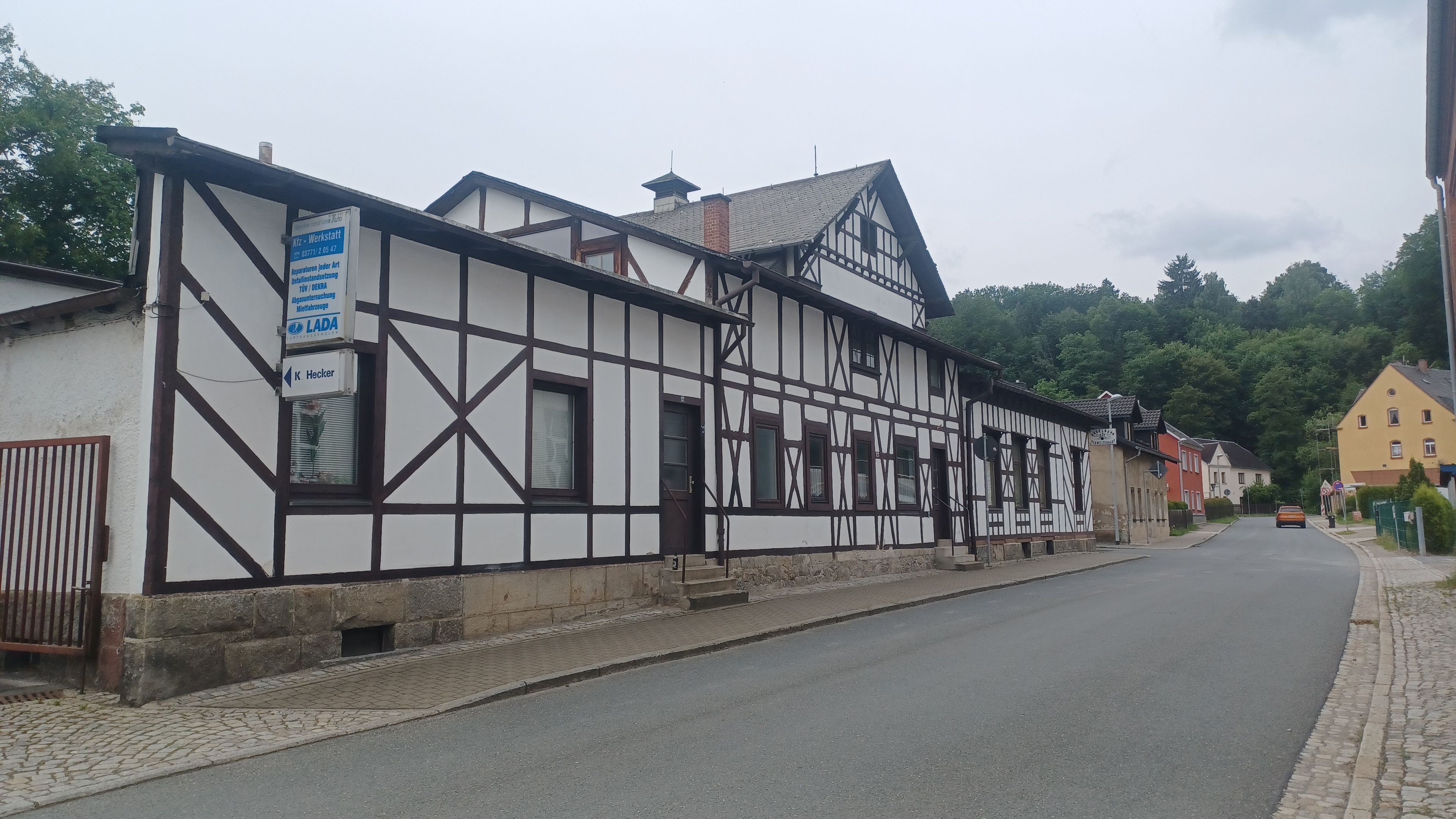 A traditional half-timbered building with a signboard, a cobblestone street, and a car parked on the side.