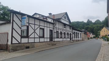 A traditional half-timbered building with a signboard, a cobblestone street, and a car parked on the side.