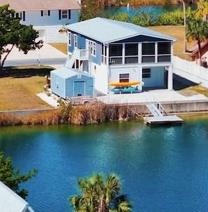 A two-story house with a dock extending into a lake, surrounded by greenery. - Waterfront Retreat + Kayaks + Game Room - Sleeps 6 (Hernando Beach)