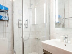 Ein modernes Badezimmer mit einer gläsernen Dusche, einem weißen Waschbecken inklusive Spiegel und einem Handtuchhalter mit blauen Handtüchern.