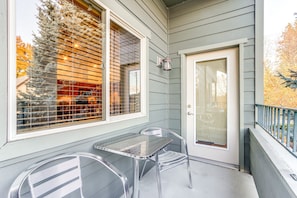 A covered porch with a table and chairs, a door, and a window with blinds.