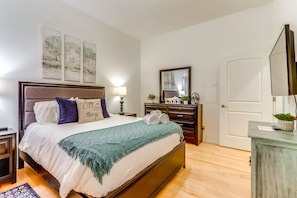 A hotel room with a bed, bedside table, lamp, dresser, mirror, and artwork on the wall. - Charming Condo in the Heart of CDA, Walking Distance to Lake (Coeur d'Alene)