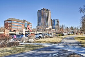 A parking lot with cars, a pedestrian pathway, and buildings including a multi-story office building and a residential high-rise. - Charming Condo in the Heart of CDA, Walking Distance to Lake (Coeur d'Alene)