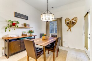 A dining area with a wooden table, leather chairs, a hanging light fixture, and decorative items on shelves.