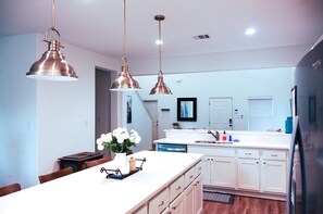 Una cocina moderna con iluminación colgante, una isla central y un comedor con sillas.