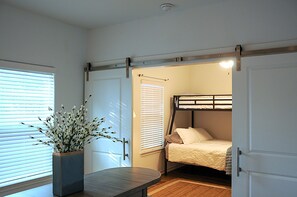 Habitación compacta con literas, una mesita con un florero y una puerta que da a otra habitación.