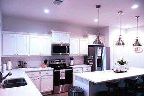 Une cuisine moderne avec des armoires blanches, des appareils en acier inoxydable et des luminaires suspendus.