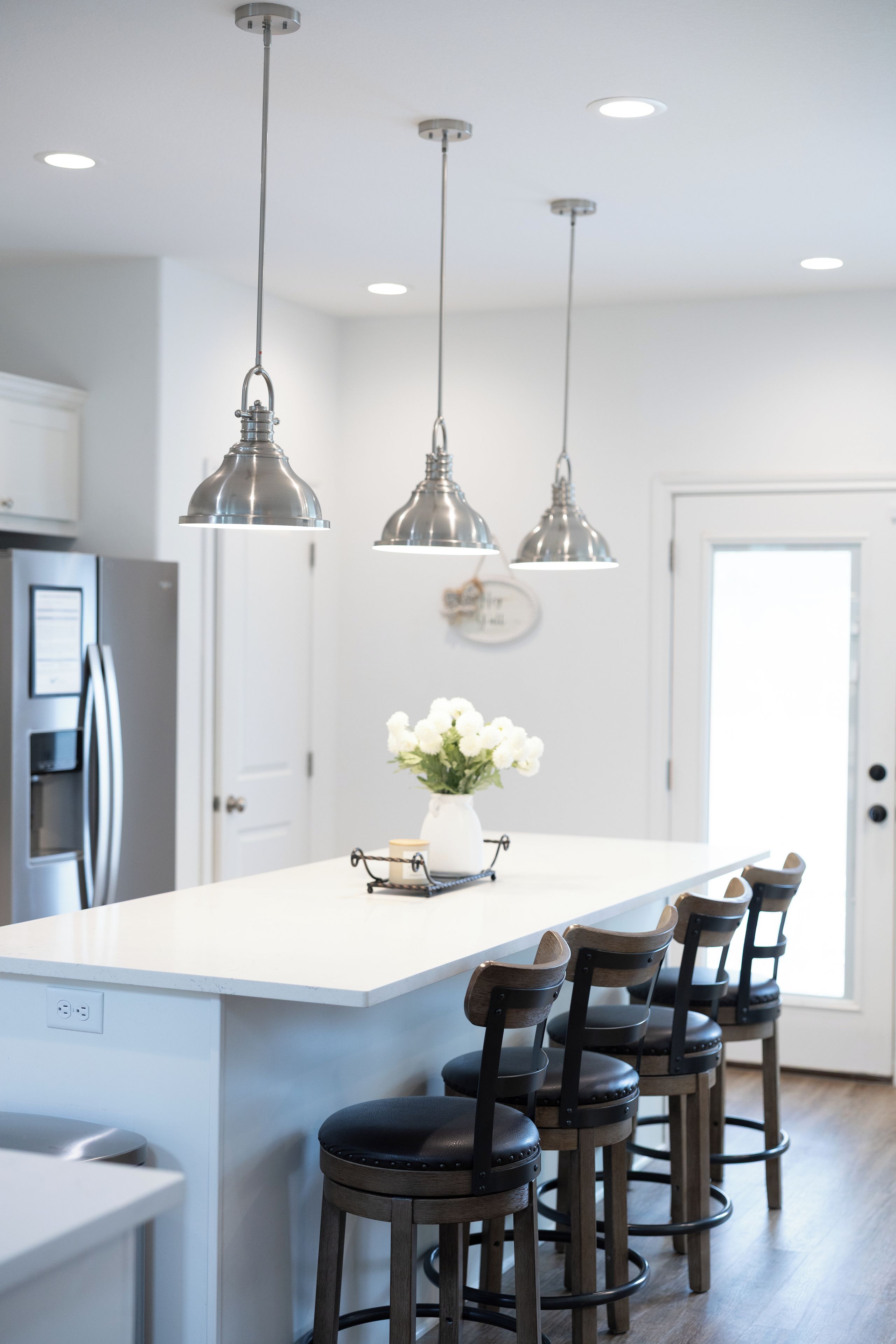 A modern kitchen with a central island, bar stools, pendant lighting, and a refrigerator.