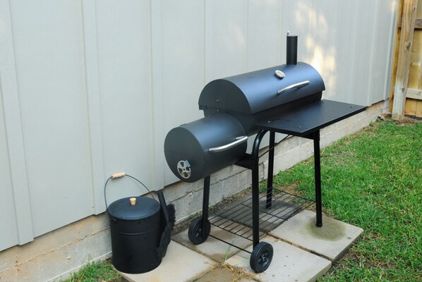 A portable barbecue grill with a side burner and a trash can.