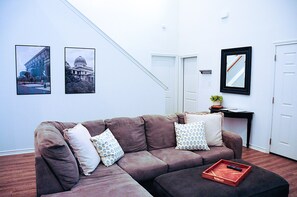 A living room with a brown sofa, two patterned pillows, a tray with a remote control, and framed pictures on the wall.