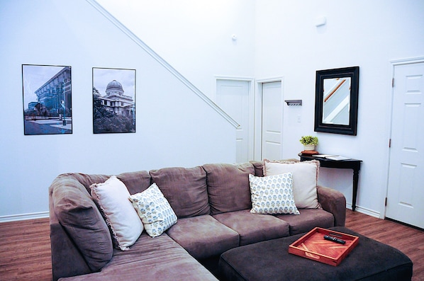 Un salon avec un canapé marron, deux coussins à motifs, un plateau contenant une télécommande et des tableaux encadrés accrochés au mur.